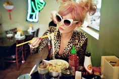 a woman sitting at a table with chopsticks in her mouth while eating food