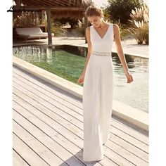 a woman in a white dress is standing on a wooden deck near a swimming pool