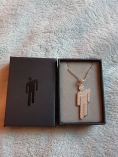 an open box with a necklace in it on a white carpeted surface next to a black box