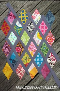 a quilted wall hanging made out of different colored fabrics and fabric strips on a wooden surface