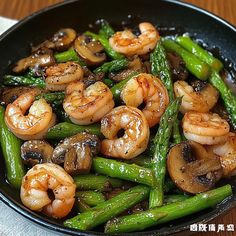 stir fry with shrimp, mushrooms and asparagus in a black pan on a wooden table