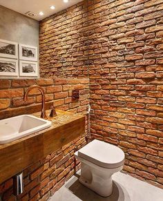 a bathroom with a brick wall and white toilet next to a wooden sink counter top