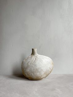 a white vase sitting on top of a table next to a gray wall and floor