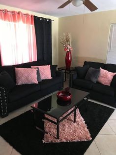 a living room with black couches and pink pillows on the rug in front of the window