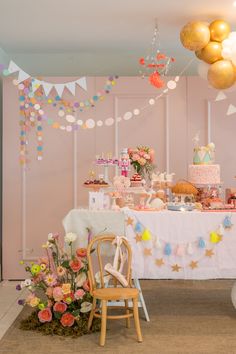 a table topped with lots of cakes and desserts next to balloons hanging from the ceiling