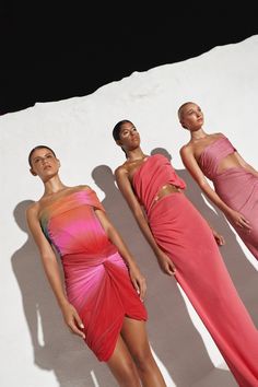 three women in long dresses standing next to each other on a white surface with shadows