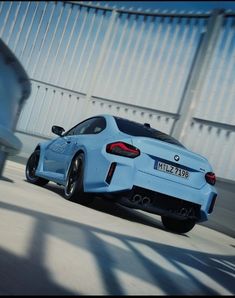 a blue sports car driving down a road next to a tall white building in the background