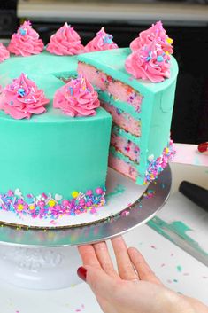 a cake with pink frosting and sprinkles is being cut by someone