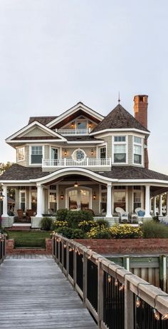 a large white house sitting on top of a lush green field next to a wooden bridge