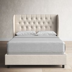 an upholstered bed with white sheets and pillows