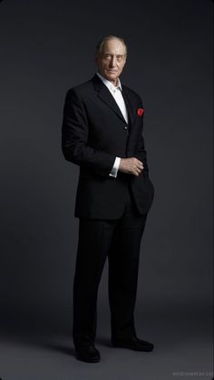 an older man in a tuxedo poses for a studio portrait with his hands on his hips