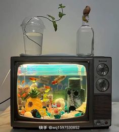 an old television with fish in it and a glass vase on the tv stand next to it