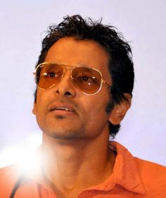 a man in an orange shirt and sunglasses looking off to the side with light shining on his face