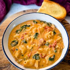 a white bowl filled with pasta and spinach on top of a wooden cutting board