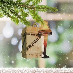 a christmas ornament hanging from a tree branch in front of a window with snow falling on it