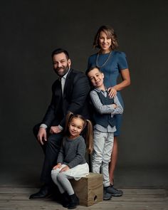 a family posing for a photo in front of a dark background with the child sitting on top of his father's chest