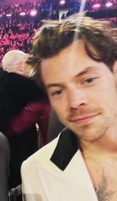 a close up of a person wearing a white suit and tie at a concert with people in the background