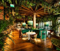 the interior of a restaurant with tables, chairs and greenery on the ceiling is lit by lamps