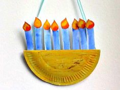 a yellow paper plate with blue and orange candles in it on a white wall background