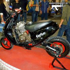 a black motorcycle on display at a show with people standing around and looking at it