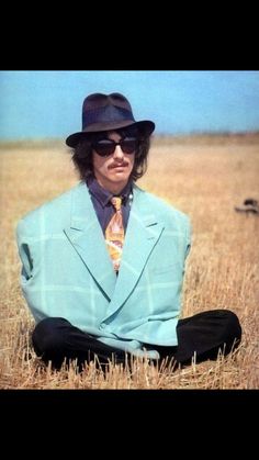 a man in a blue suit and hat sitting on the ground with his legs crossed