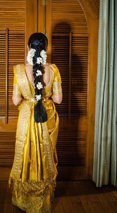 a woman wearing a yellow sari with white flowers in her hair is looking out the window