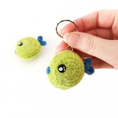 a hand holding a green keychain with two small blue fish on it's side