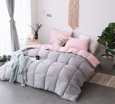 a bed with pink and grey comforters in a room next to a window, potted plant