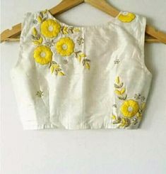 a white top with yellow flowers is hanging on a wooden hanger next to a wall