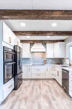 a kitchen with white cabinets and wood flooring, along with stainless steel ovens