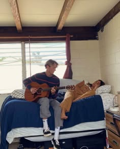 a man sitting on top of a bed next to a woman playing an acoustic guitar