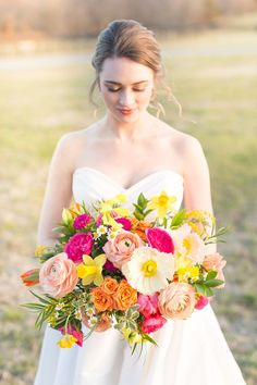 a woman in a white dress holding a bouquet of pink, yellow and orange flowers