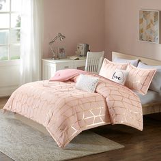 a bed with pink comforter and pillows on top of it in a bedroom next to a window