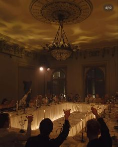 a group of people sitting at a table with candles in front of them and one person raising their hands