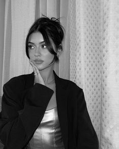 a black and white photo of a woman leaning against a curtain with her hand on her face