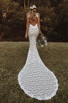 a woman in a white wedding dress is standing on the grass with her back to the camera