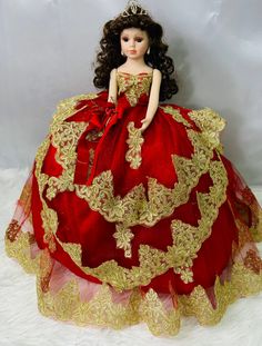 a doll dressed in a red and gold gown on a white blanket with a tiara