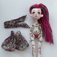 a doll with pink dreadlocks next to it's accessories on a white surface