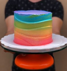 a rainbow cake sitting on top of a white plate next to a person's hand