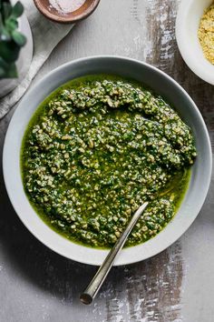 a white bowl filled with green pesto next to two bowls of yellow and red spices