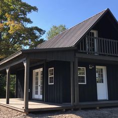 a small black cabin with white doors and windows on the front porch is surrounded by trees