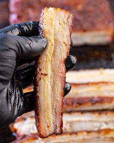 a person in black gloves holding up a piece of bacon