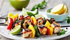 chicken kabobs with peppers and limes on a white plate