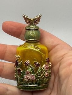 a hand holding a small glass bottle with flowers on it