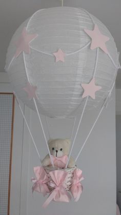 a teddy bear in a hot air balloon with pink bows and stars hanging from the ceiling