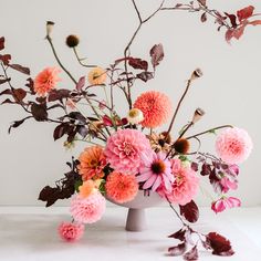 a vase filled with lots of pink and orange flowers on top of a white table