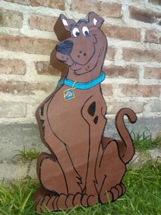 a wooden cutout of a dog sitting in the grass next to a brick wall