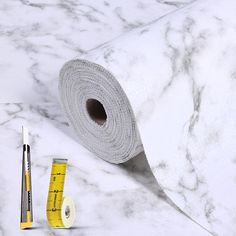 a roll of white marble paper next to a measuring tape and ruler on a table