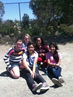 a group of young women sitting on top of a dirt field next to each other