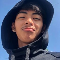 a young man wearing a black hat and hoodie looking at the camera with a blue sky in the background